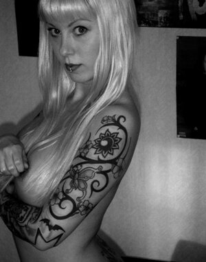 Blonde lady with tattooed body poses undressed in the black and also white